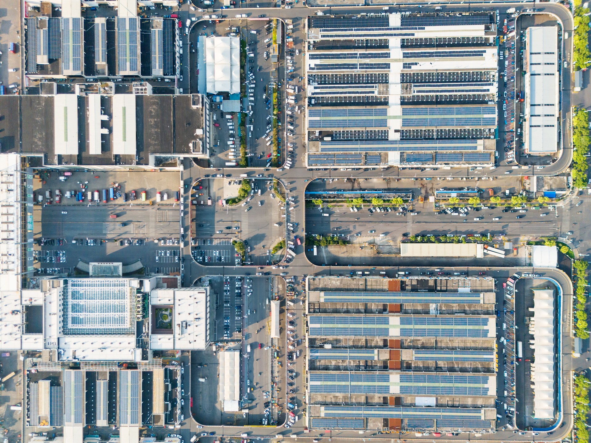 An aerial view of a large distribution warehouse with solar cells on its roof and trucks parked outside.
